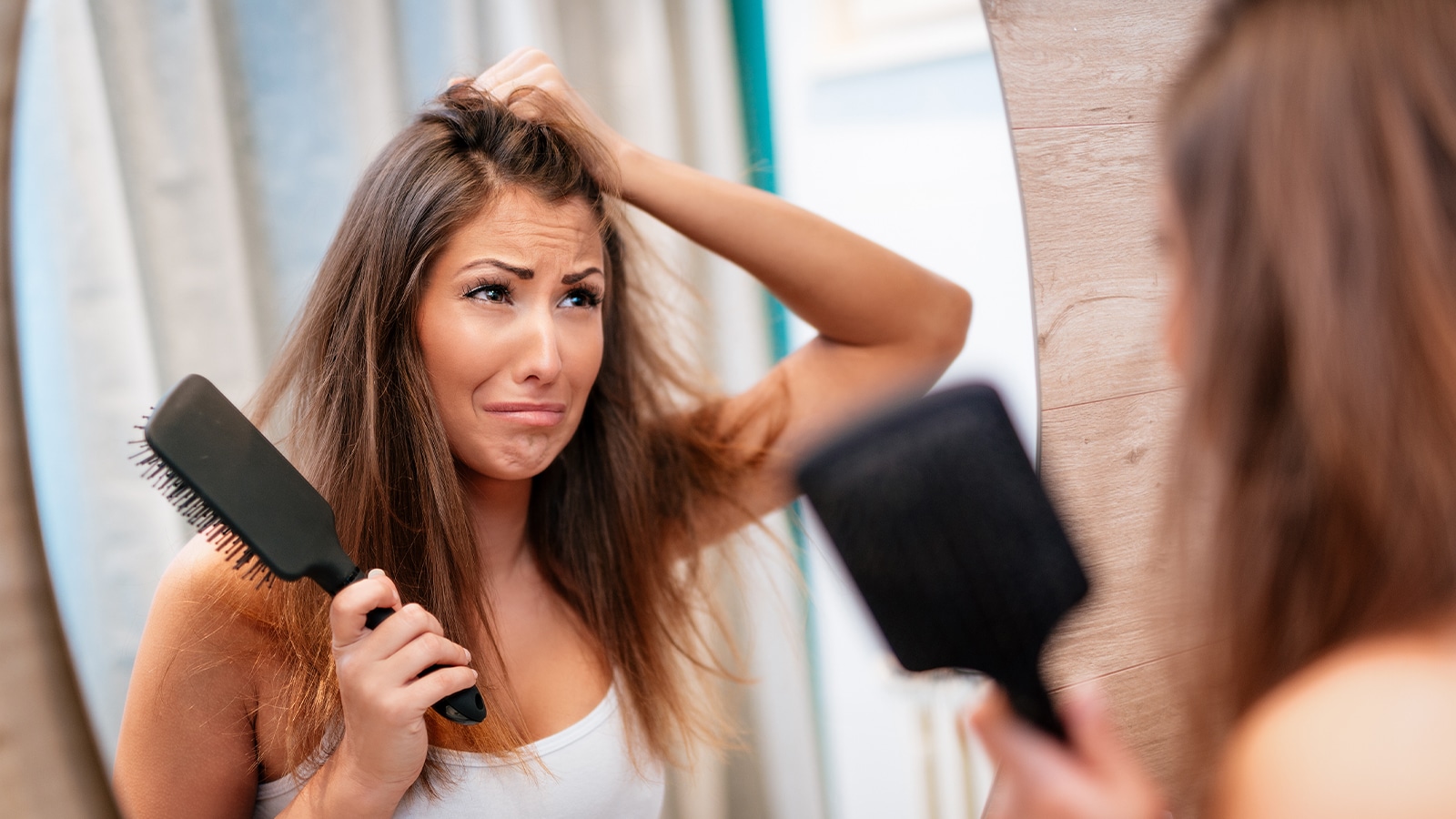 Woman with extensions seeing product residue in her hair in the mirror